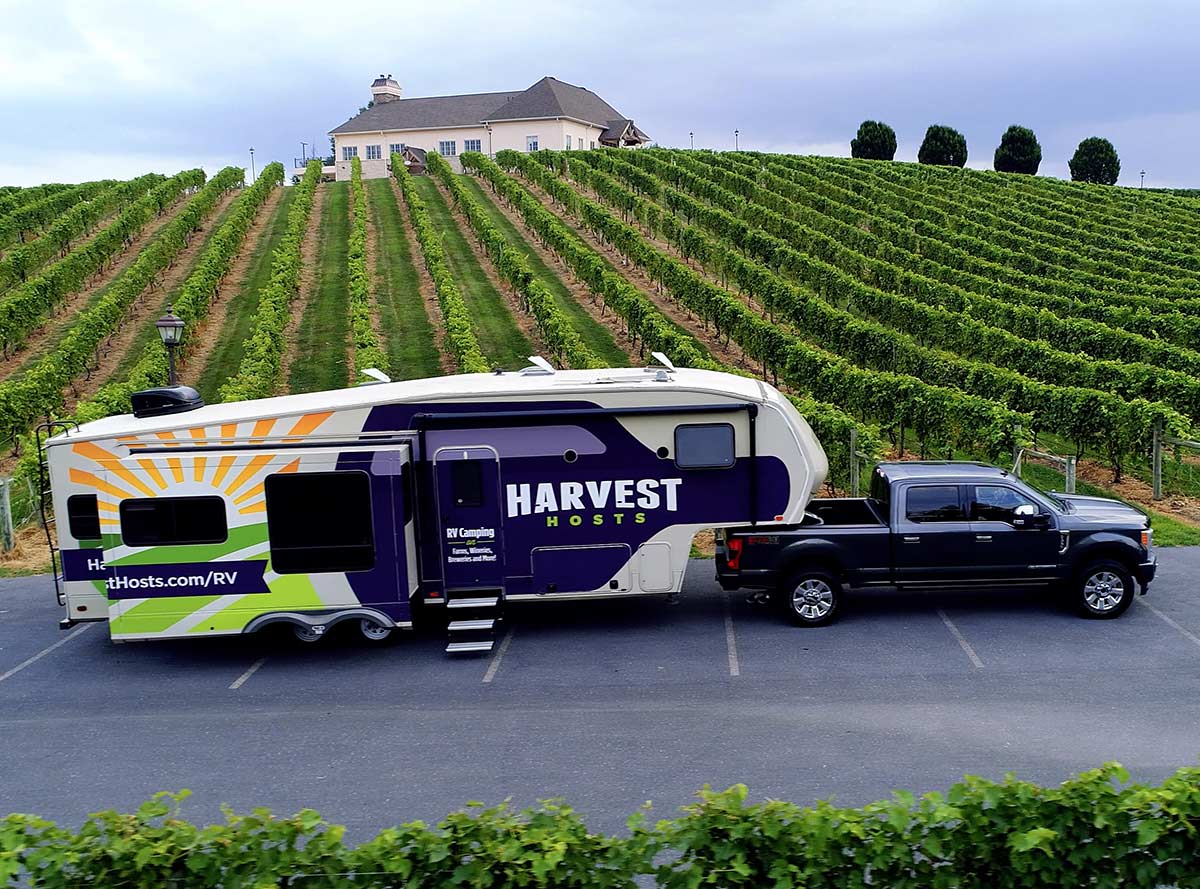 Harvest Hosts RV being pulled by a black truck by rows of grapes