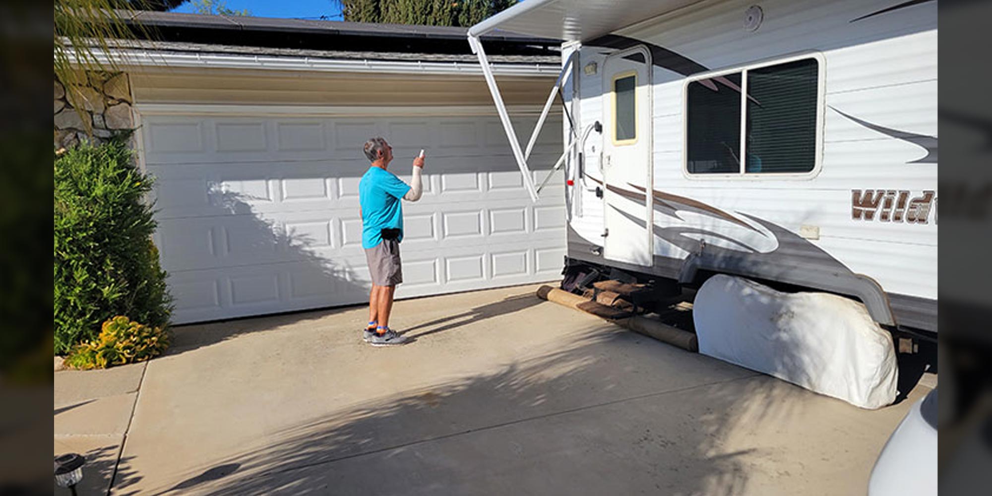 a man powers the remote control awning of an RV trailer parked in a residential driveway