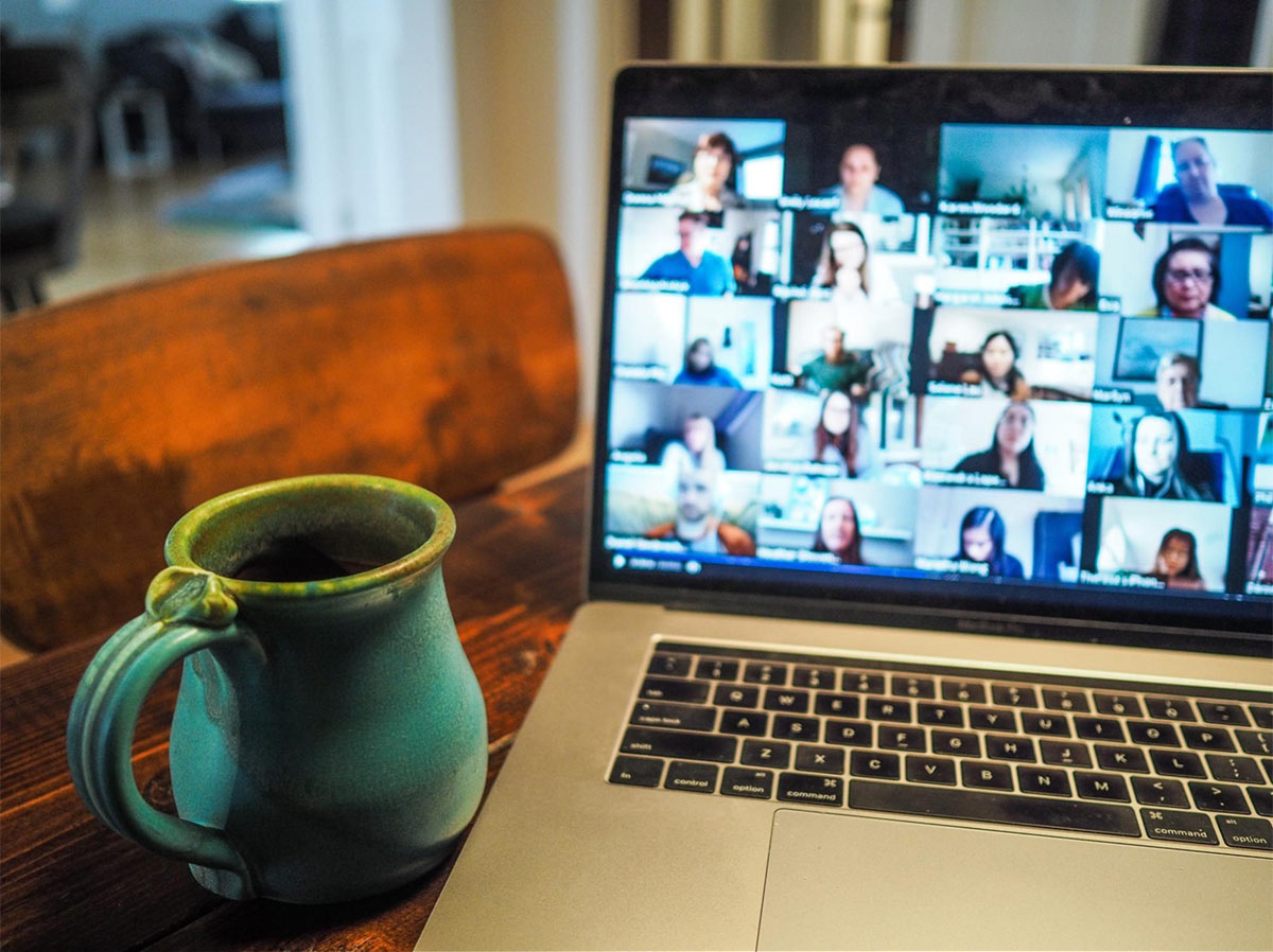 a computer showing a lot of people on a zoom call with a blue-green coffee cup next to it