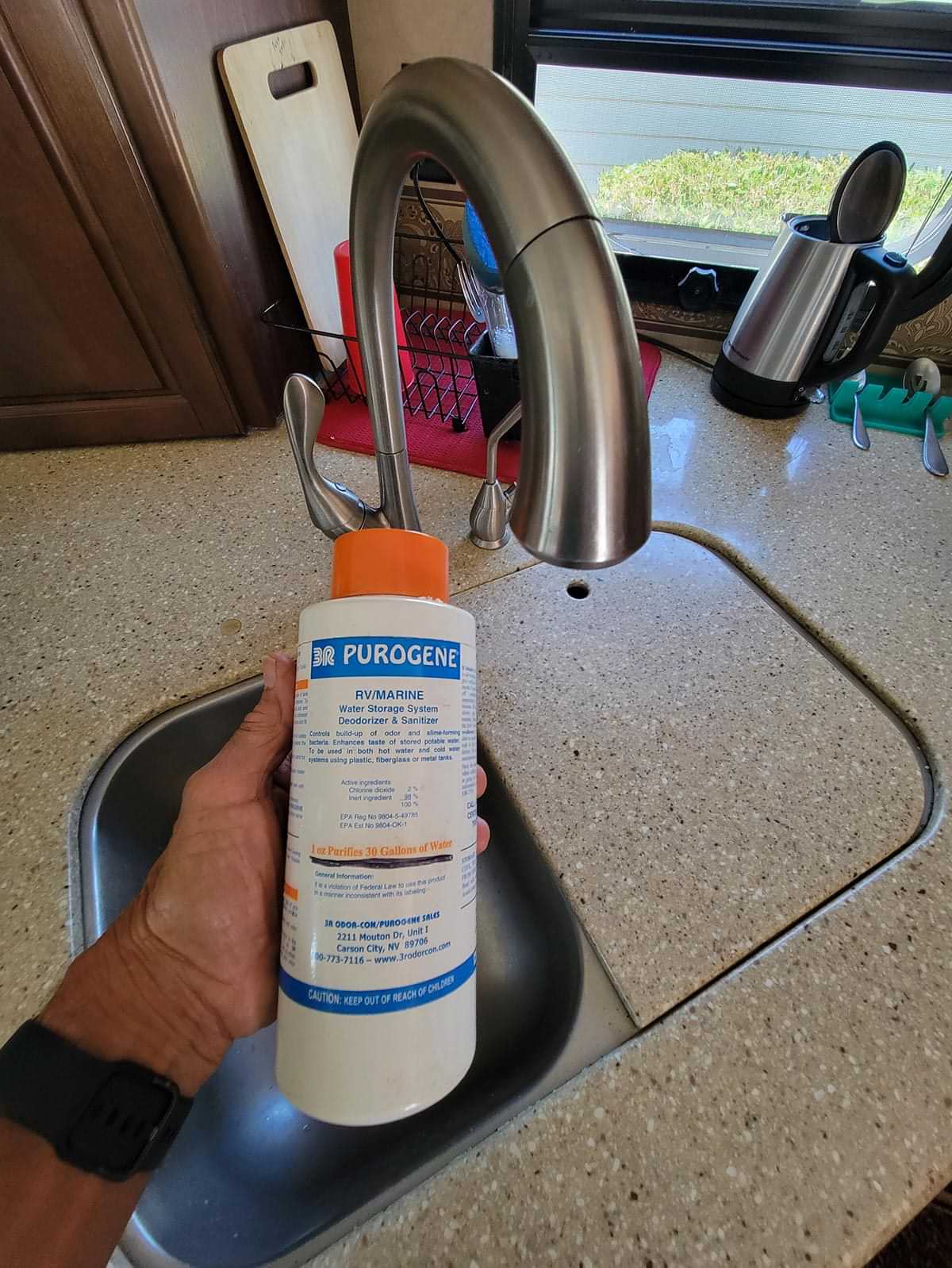 mechanic holds a container of Purogene water treatment in hand while standing at an RV sink