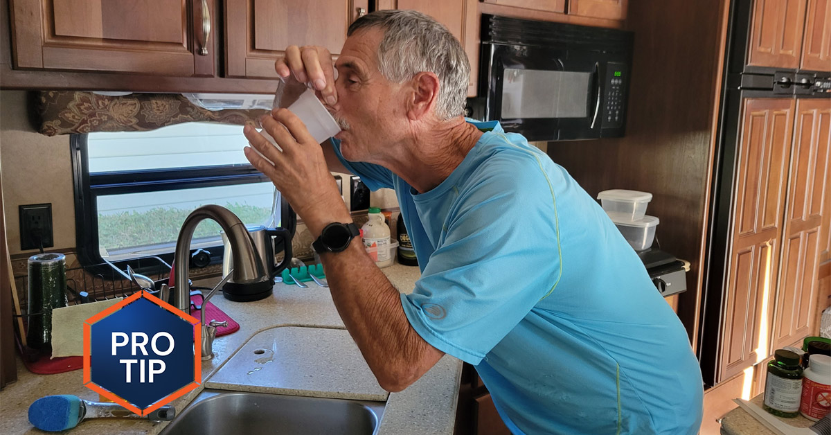 man standing at an RV sink holds his nose while drinking from water from a plastic cup