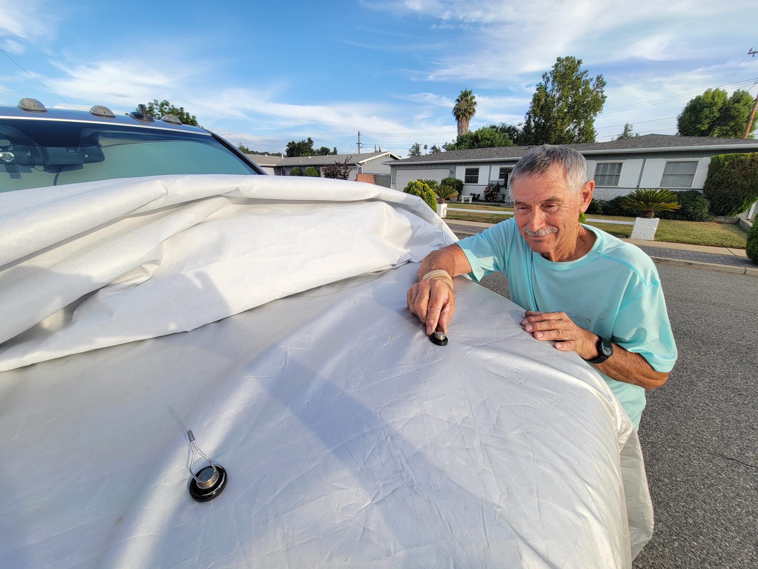 RV technician places magnets to anchor the car cover on the front section of the truck