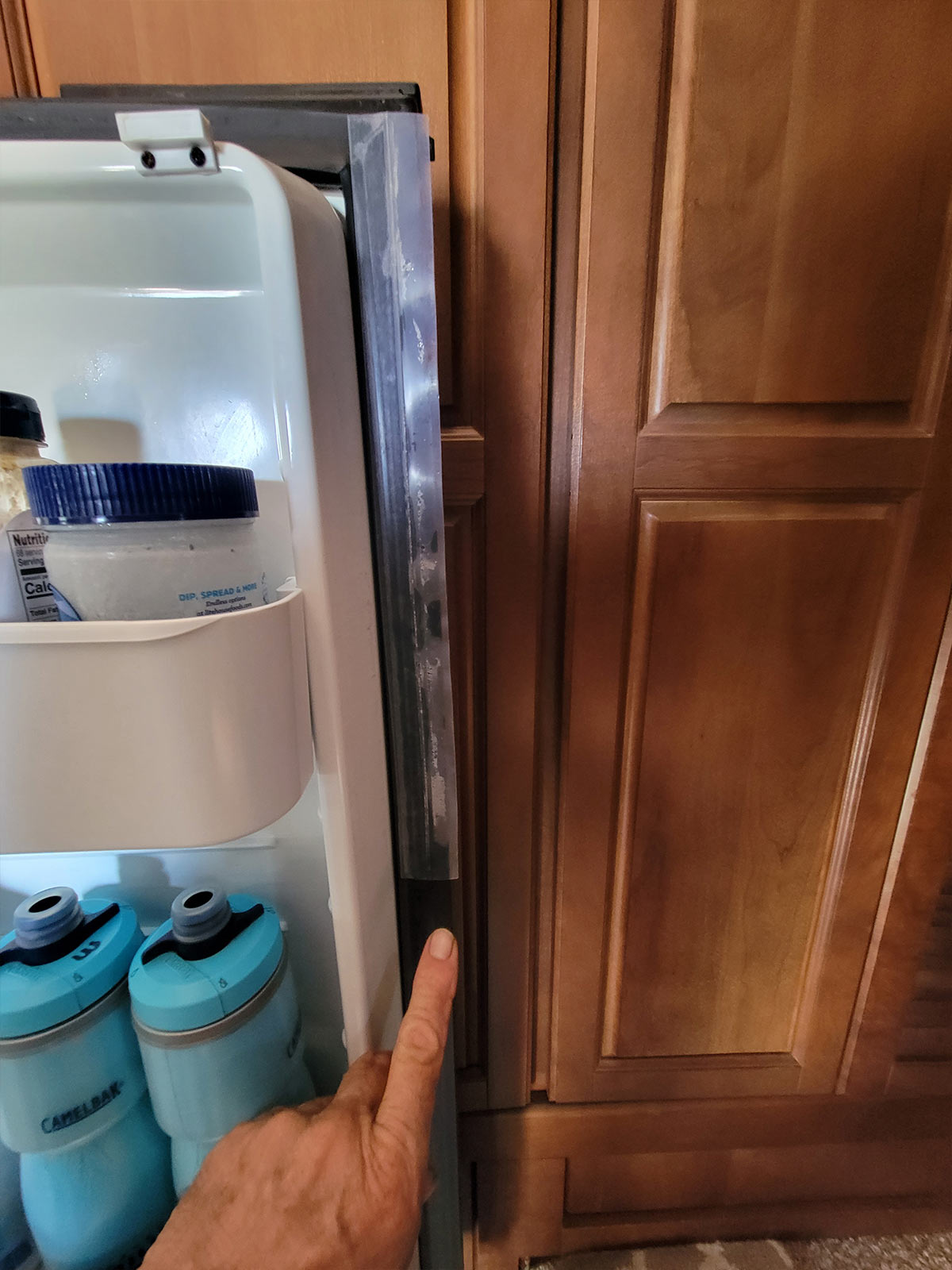 a finger gestures to another area on the refrigerator that required gasket repair with a larger section of silicone seal tape
