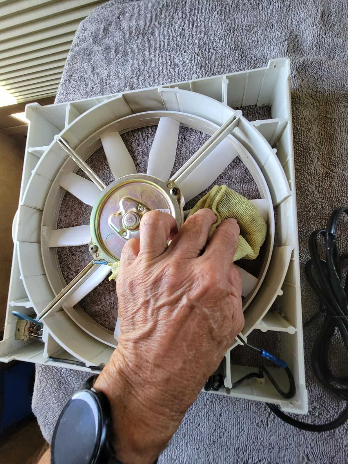 a hand uses a microfiber cloth to clean the exposed blades of the fan