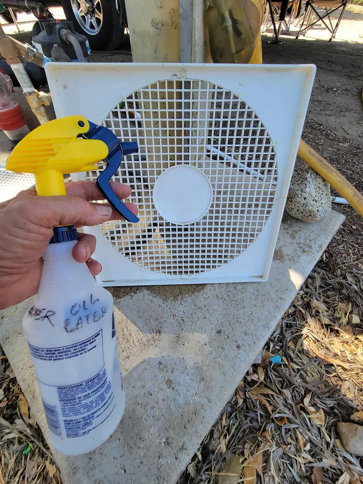 a hand holds a spray bottle in preparation to clean the fans blade protecting cover