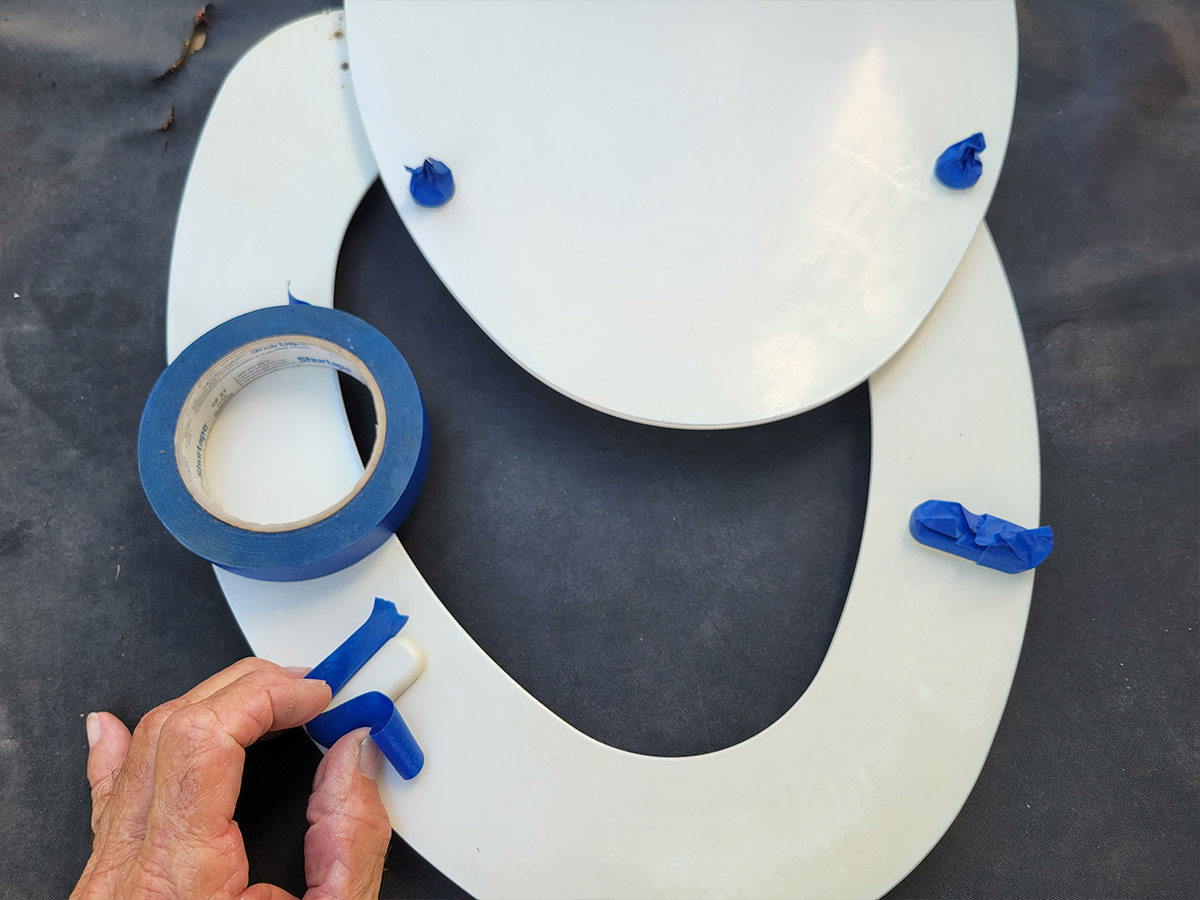 the toilet seats plastic bumpers are masked with tape in preparation for painting