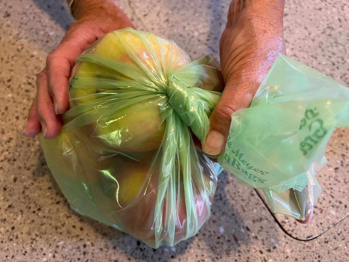 the opening of the x-large Debbie Meyer Green Bag filled with apples is twisted closed