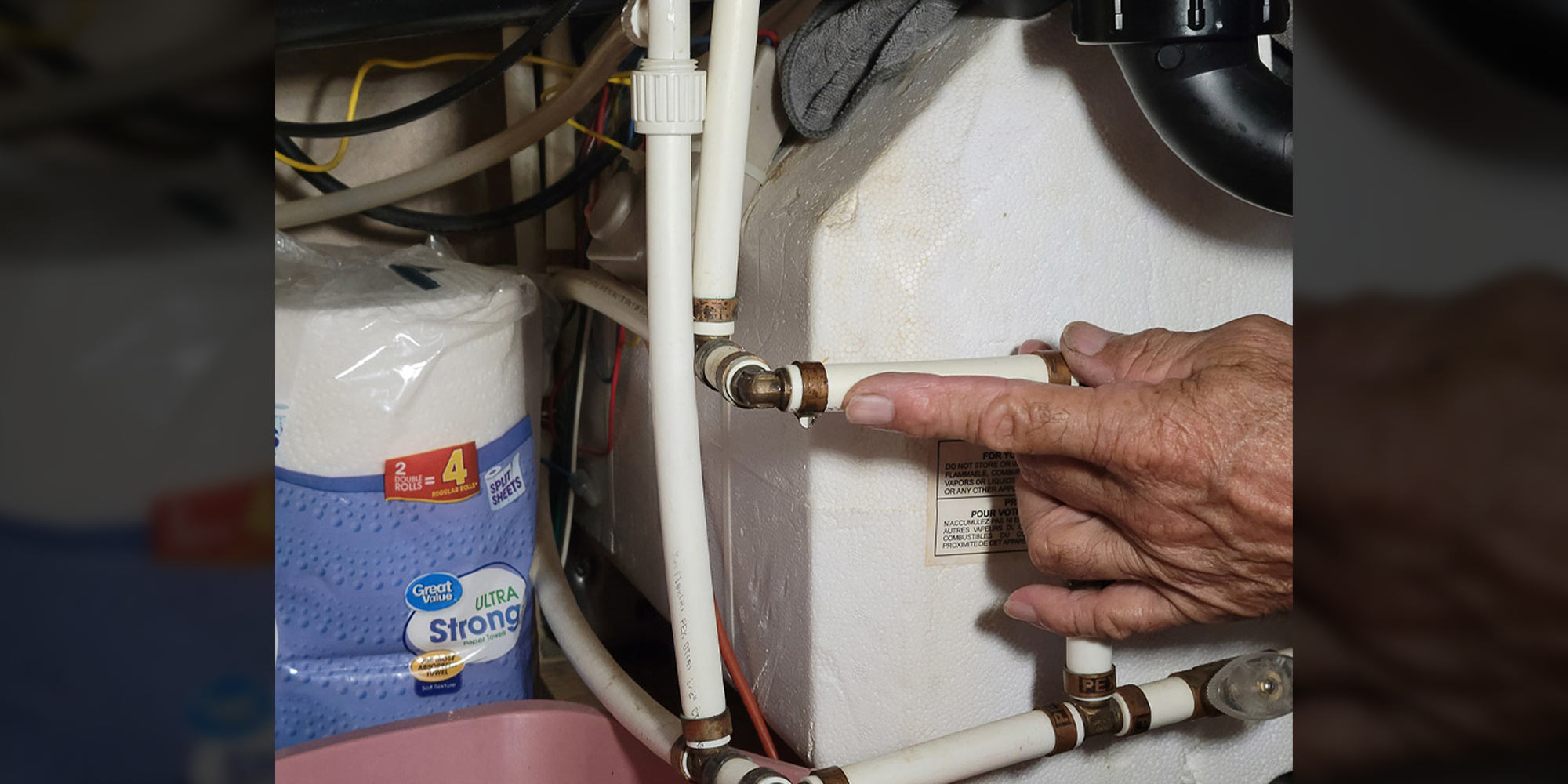a hand points to a leaking pipe in an RV water system