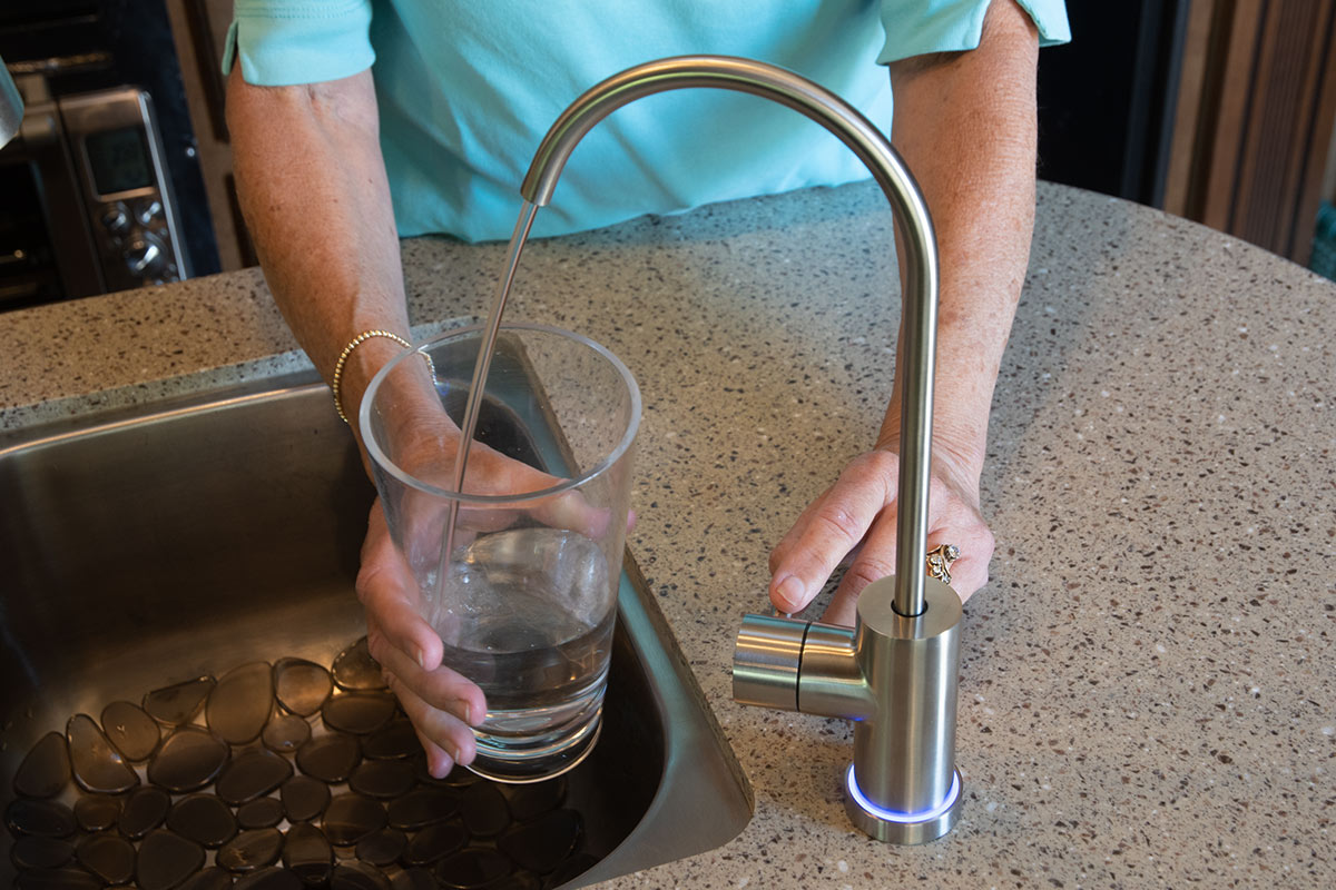 a hand holds a cup filling with water from the Acuva Filter spigot