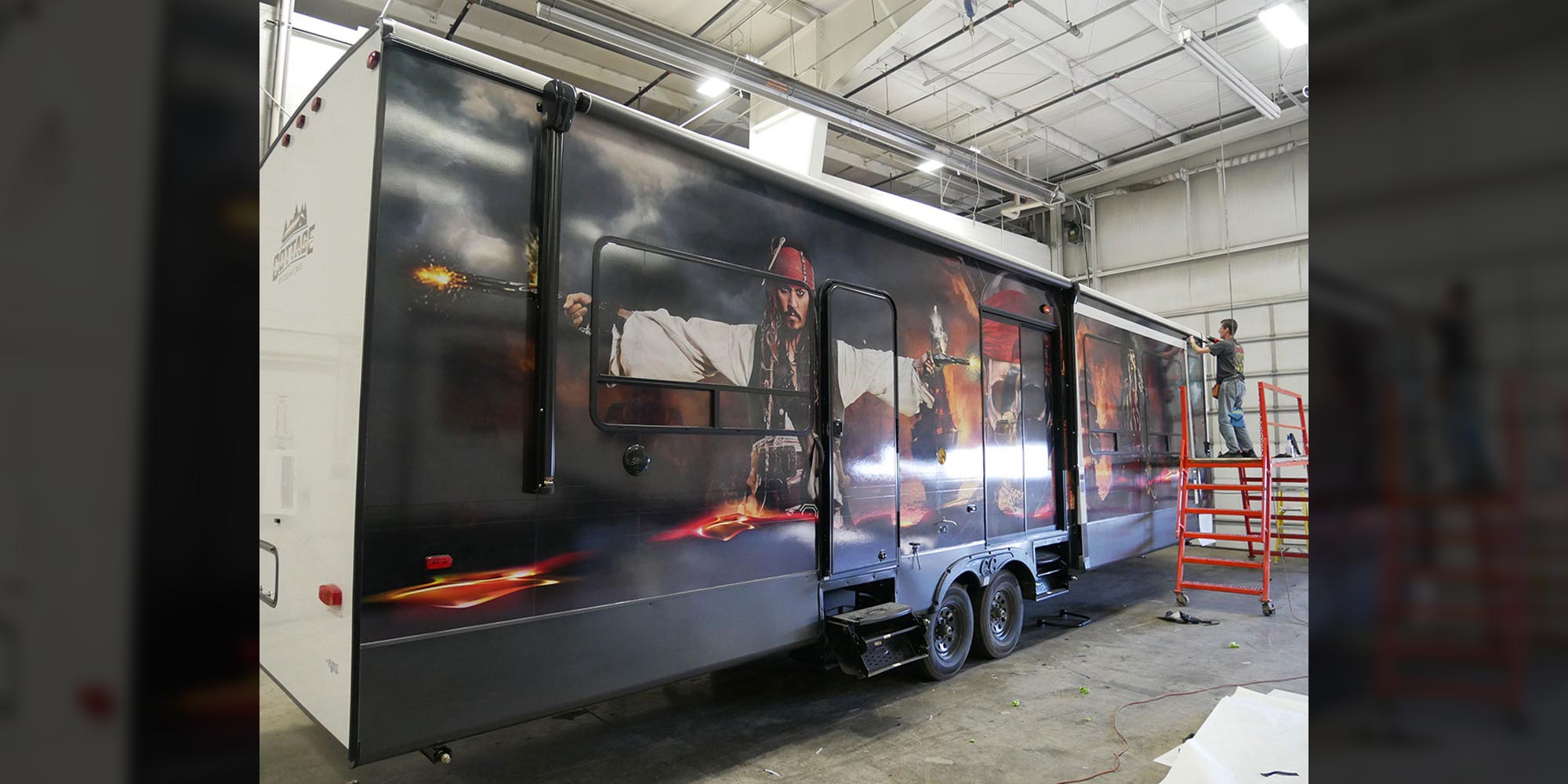 a man stands on a lift next to an RV with a Pirates of the Caribbean wrap