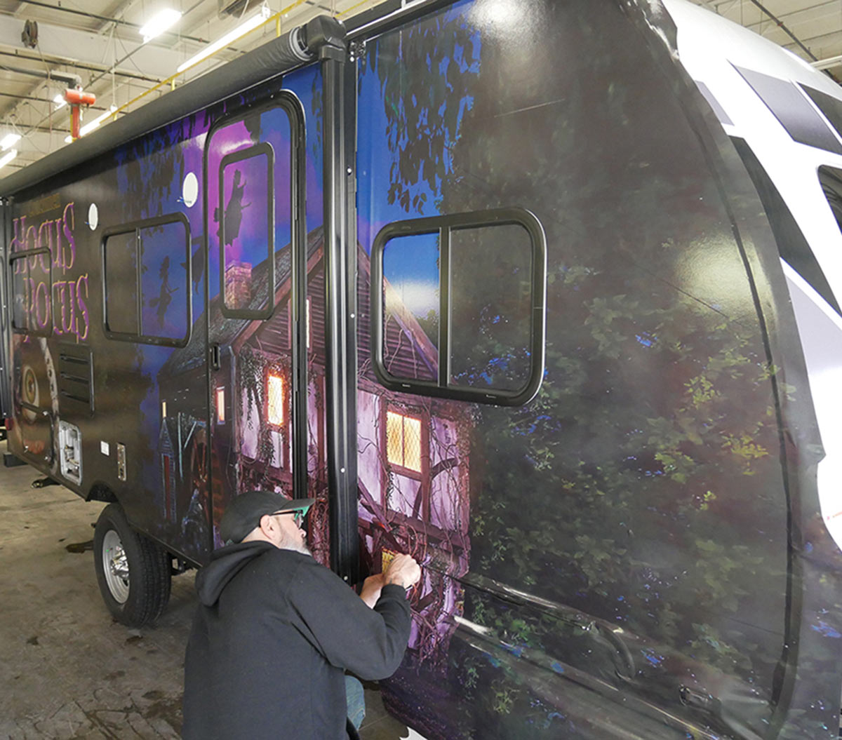 a man works on a Hocus Pocus themed graphic wrap on a travel trailer
