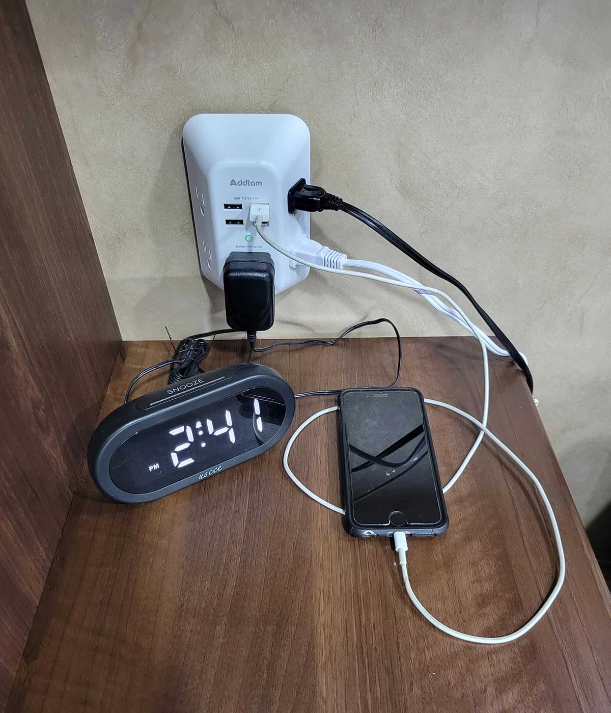 an Addtam wall charger installed at a bedside outlet and connected to a digital alarm clock and smartphone