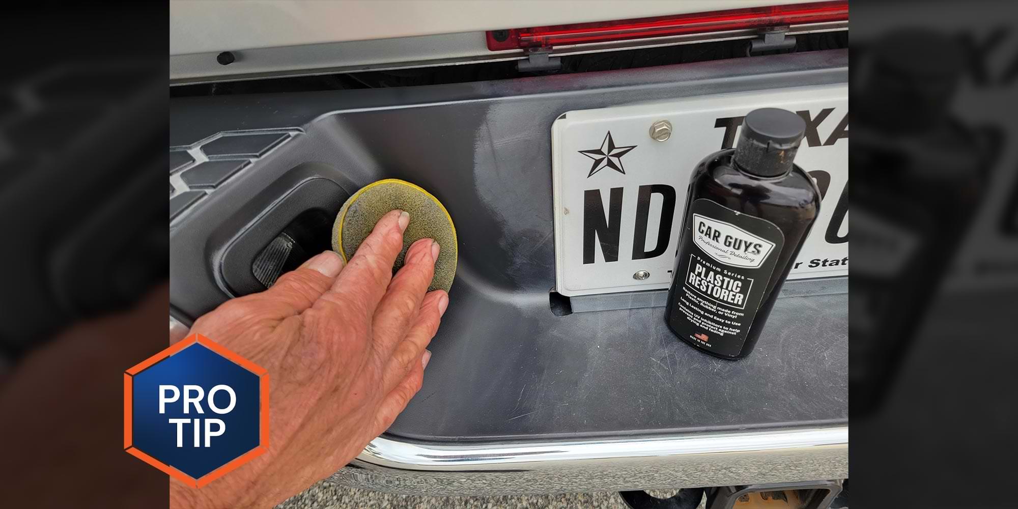 a hand uses a foam pad to wipe Plastic Restorer solution on to the plastic trim on a vehicles rear bumper