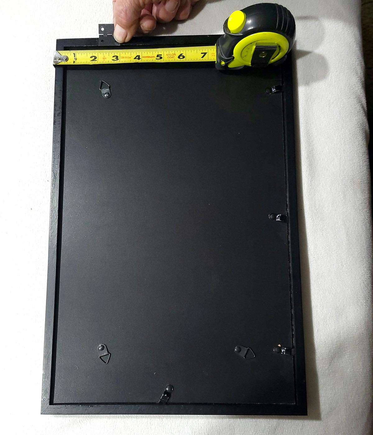 top view of a tape measure being used to locating the small hinges on the picture frame