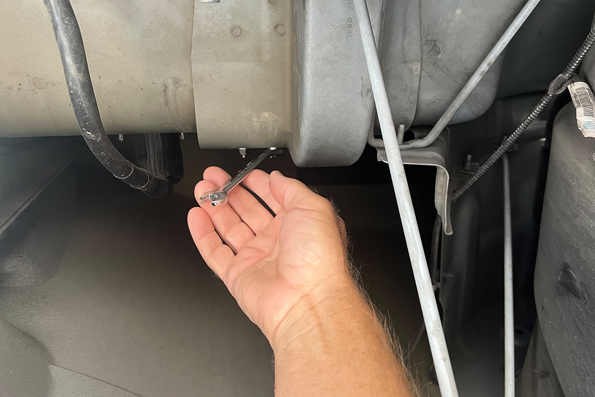 a hand uses a wrench to work a nut beneath a truck wheel well