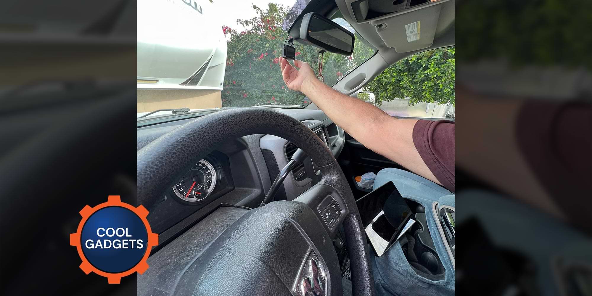 an arm reaches out to a device connected to a car windshield beneath the rear view mirror