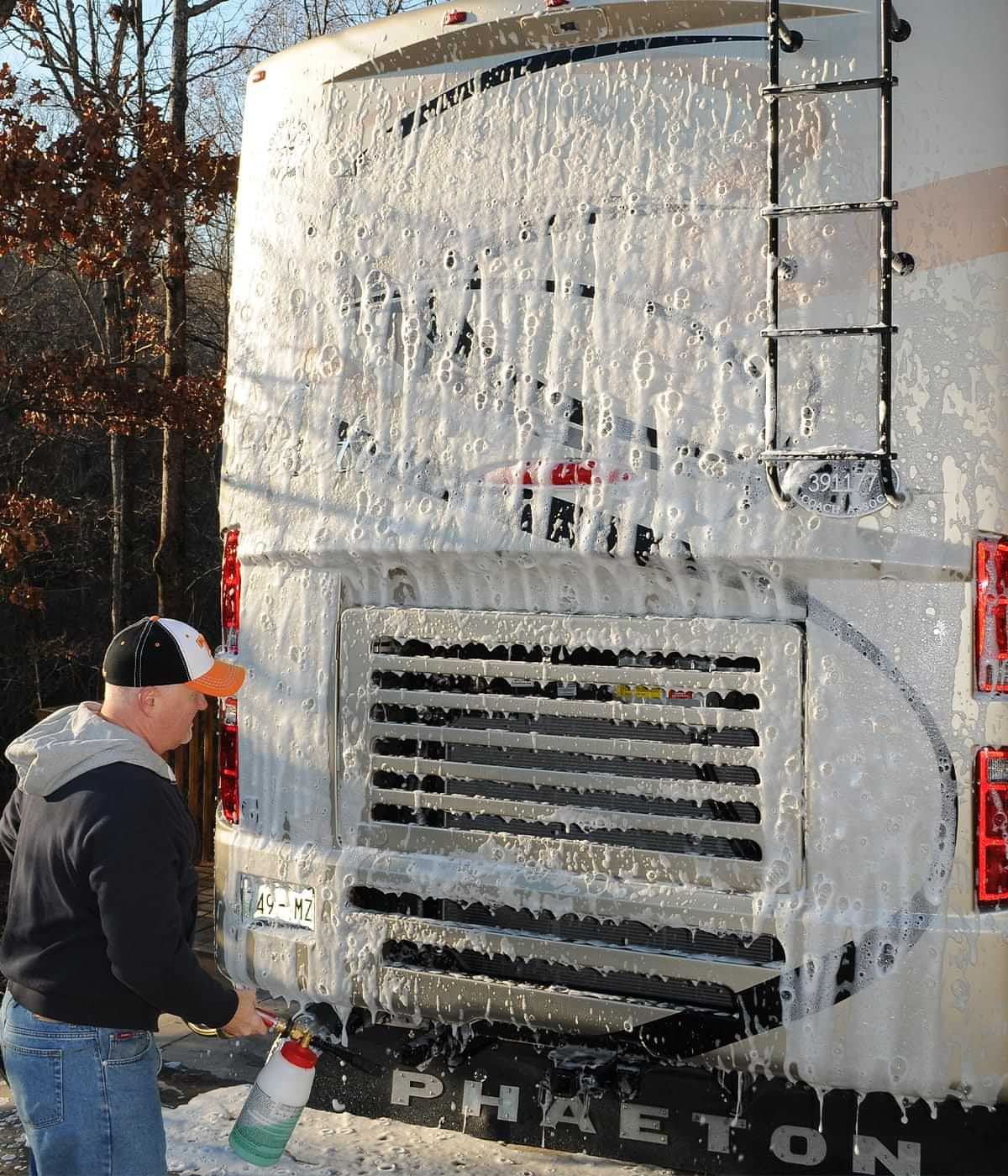 a man uses a foam gun to cover the back of an RV in foam cleaner