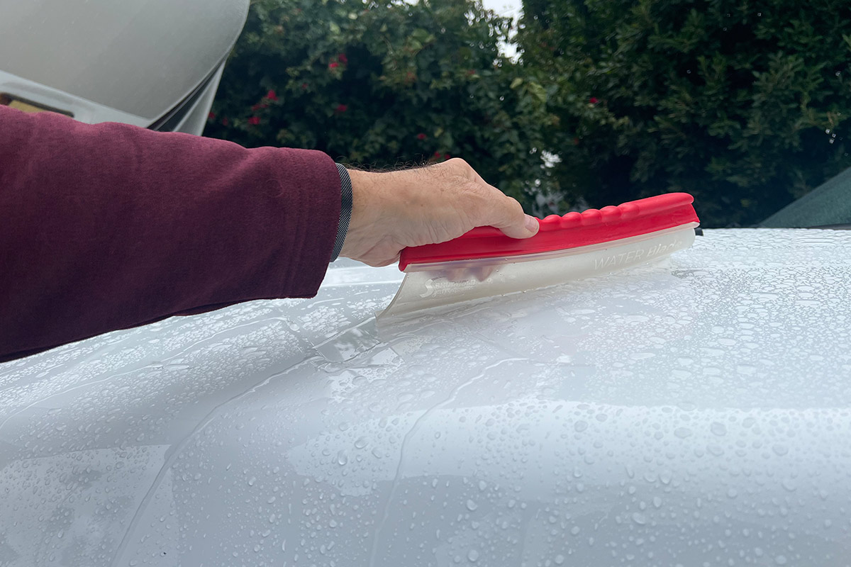 a hand grasps the Water Blade gadget and wipes water from the hood of a white vehicle