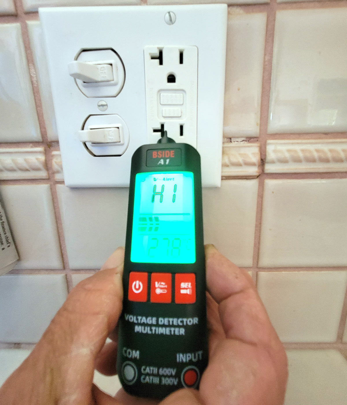 the Bside meter's screen illuminated as it is held up to a power outlet