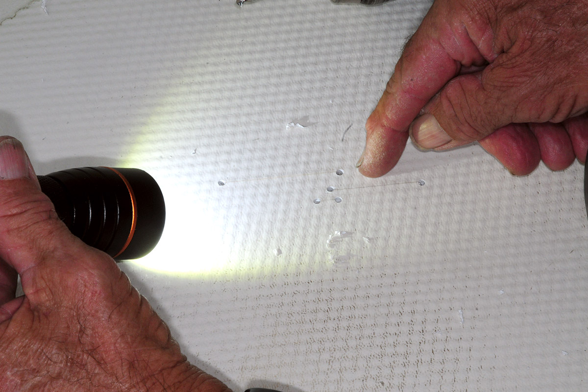 a hand holds a flashlight at an angle as a finger points to drilled holes in the shower pan
