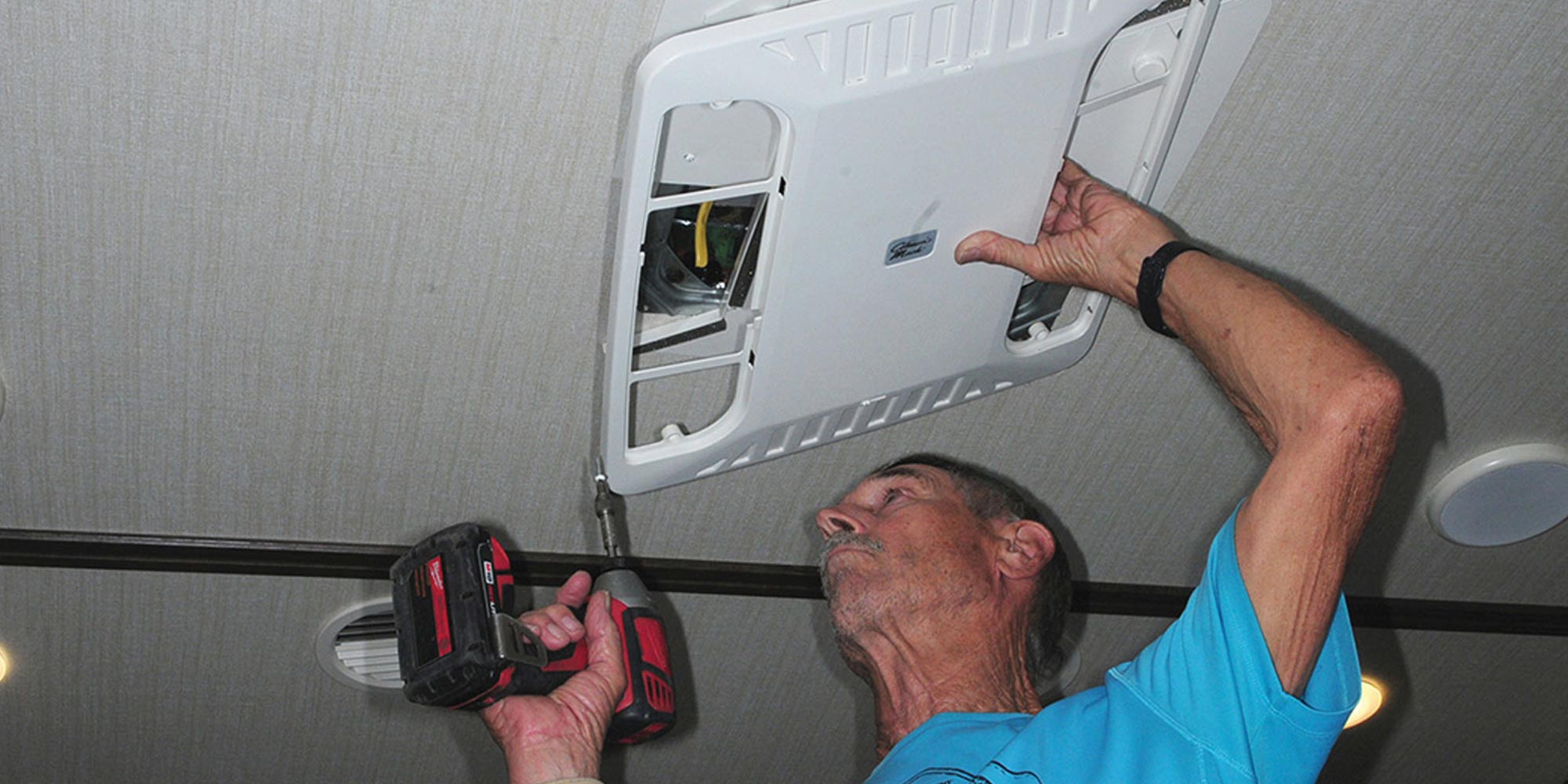 a man using a drill on a corner screw of a ceiling AC vent