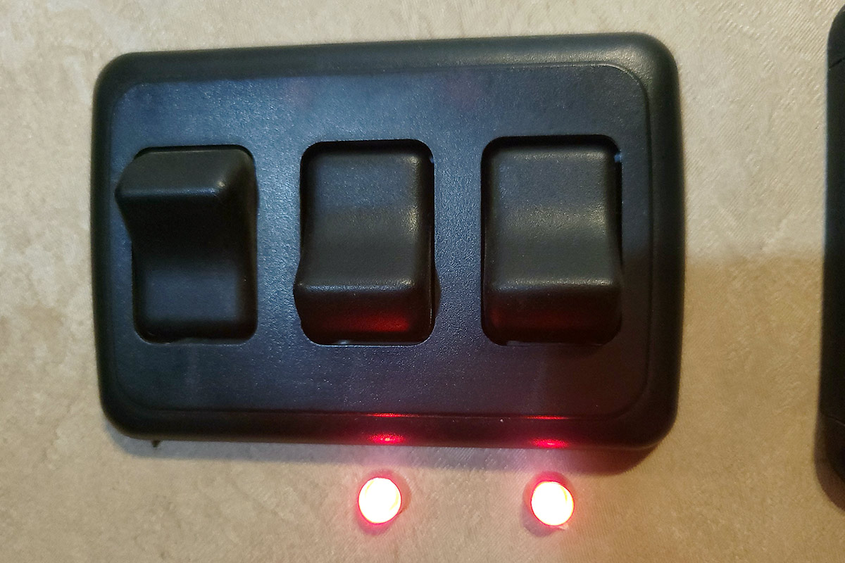 close view of a light switch with three toggles, the right two with active red indicator lights below