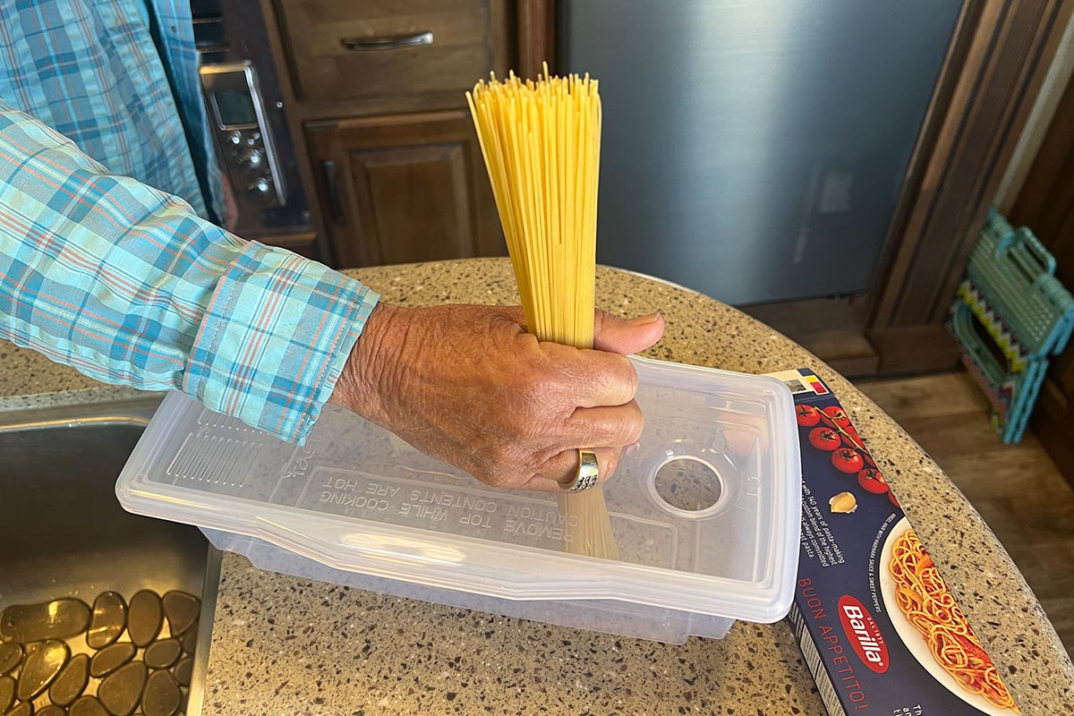 a smaller hole at the top of the rectangular container is used to measure a bundle of spaghetti noodles in a hand