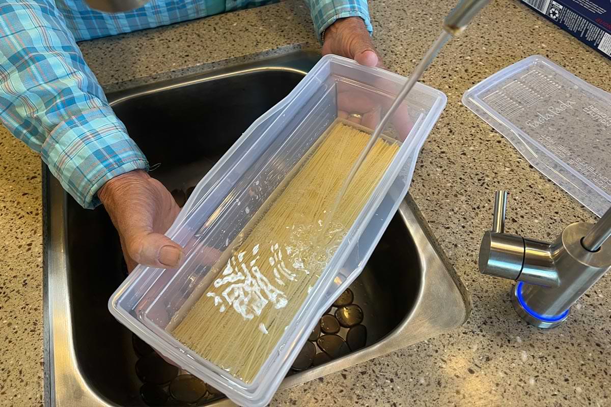 with the uncooked noodles resting at the bottom, the rectangular container is filled with water