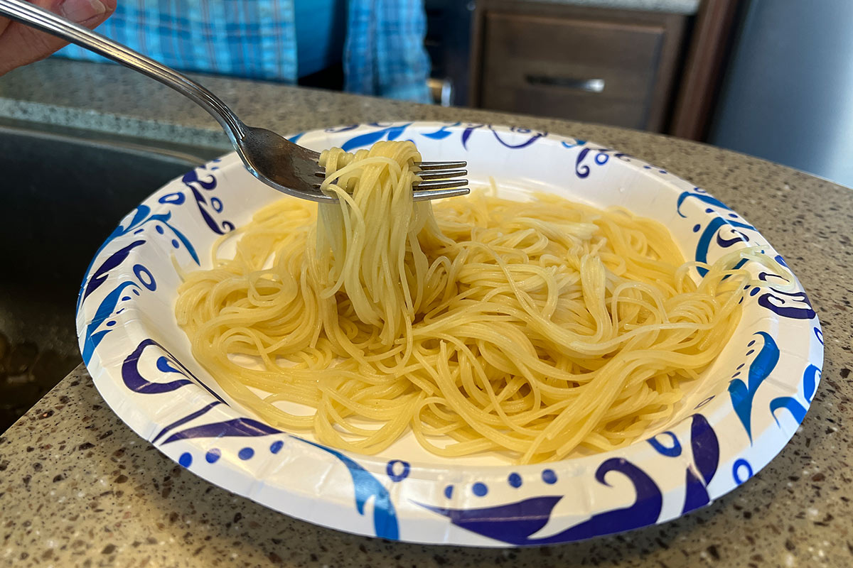close view of cooked spaghetti noodles on a paper plate and fork