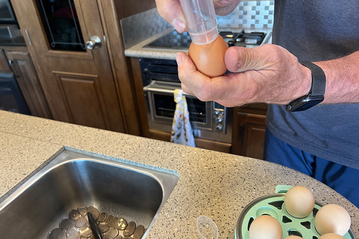 using the needle built into the base of the measuring cup, a whole is lightly punched into an egg before placing it on the boiling tray
