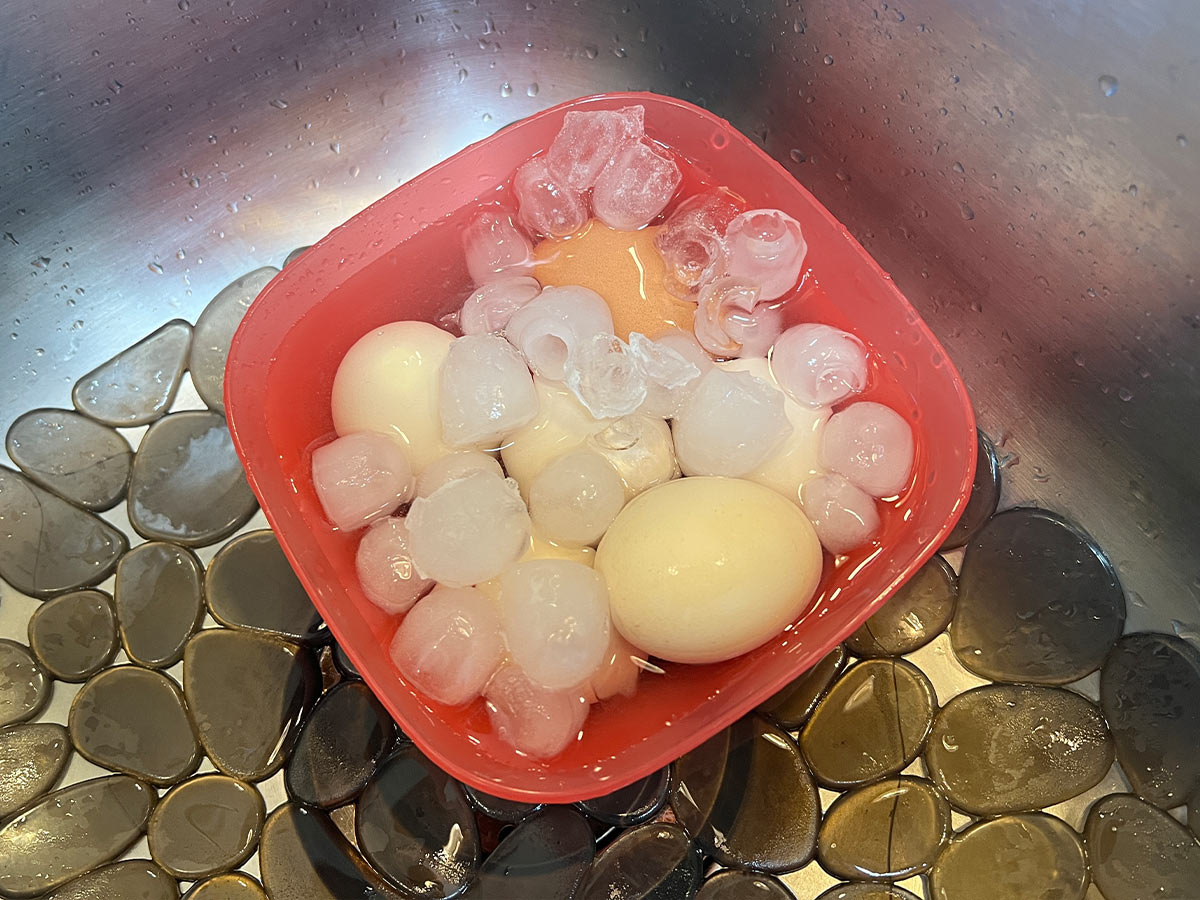 top view of a red bowl filled with boiled eggs and ice in a sink