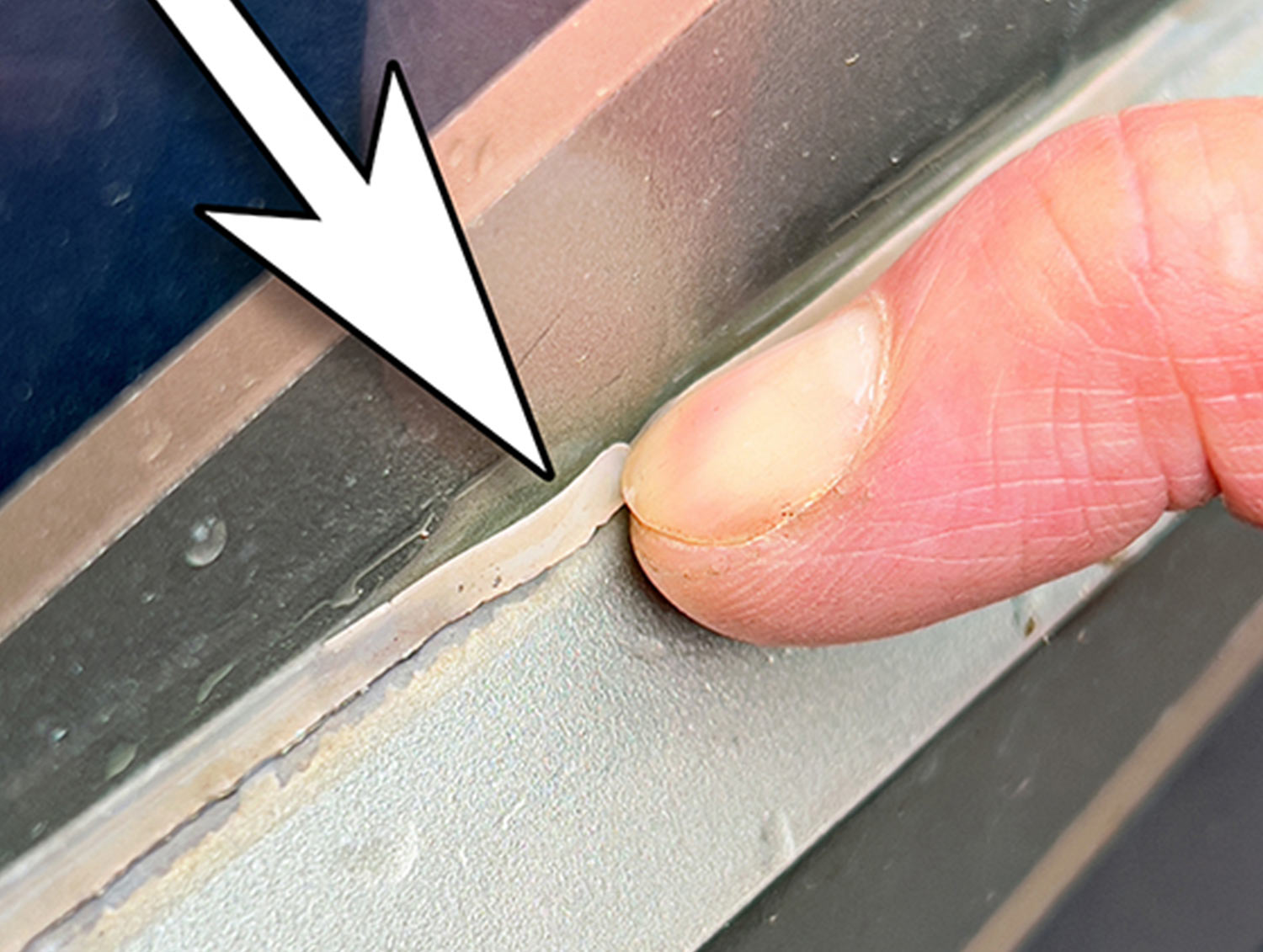close view of a finger pointing to a thin bead of sealant along an RV body molding that has come loose