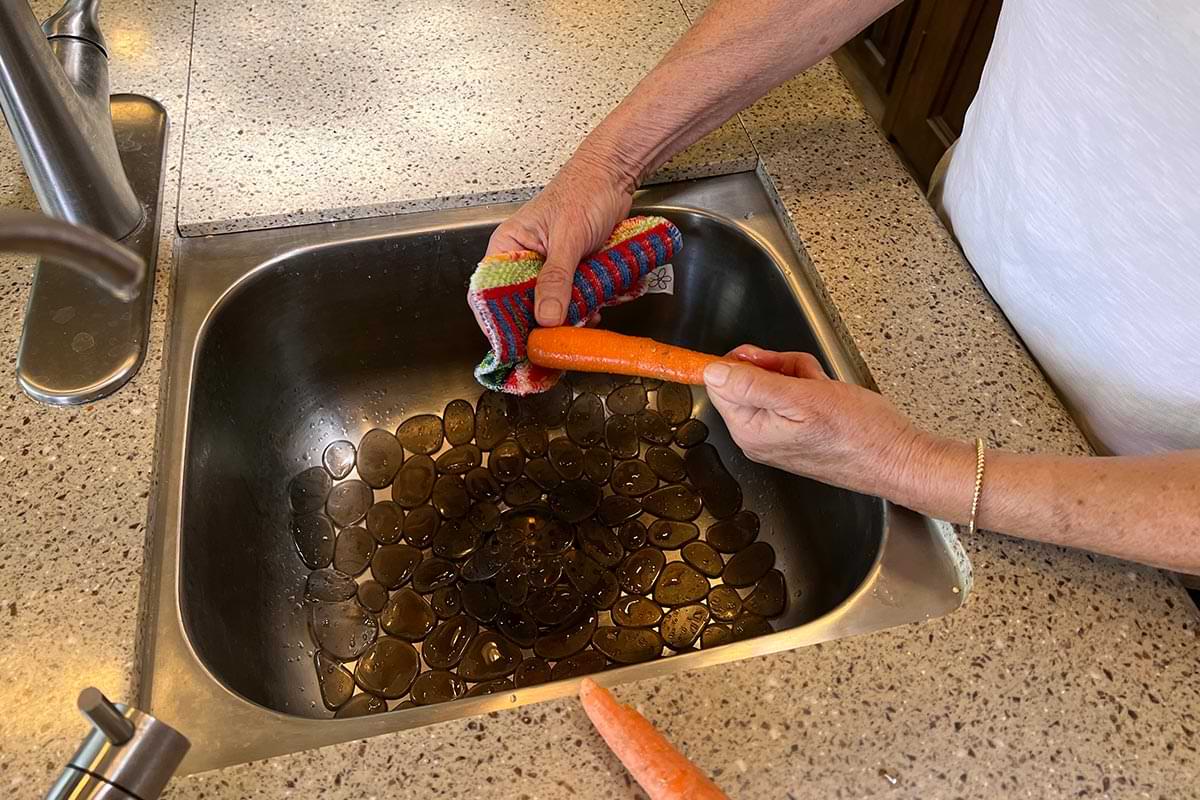 hands use a Skoy Scrub pad to clean carrots in an RV sink