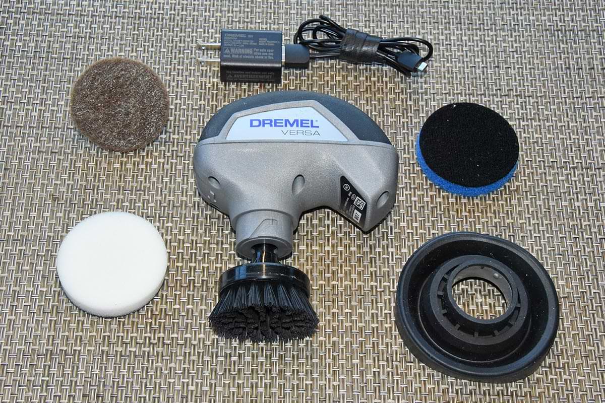 the Dremel Versa's parts and pieces organized on a surface including three cleaning pads for specific purposes, a base for the pad, a bristle brush and a rubber splash guard