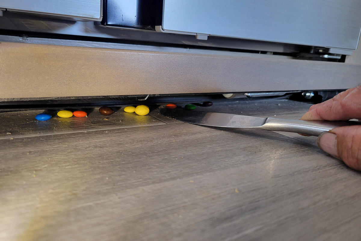 a dull knife in hand is used to coax loose M&Ms from beneath an RV slide out
