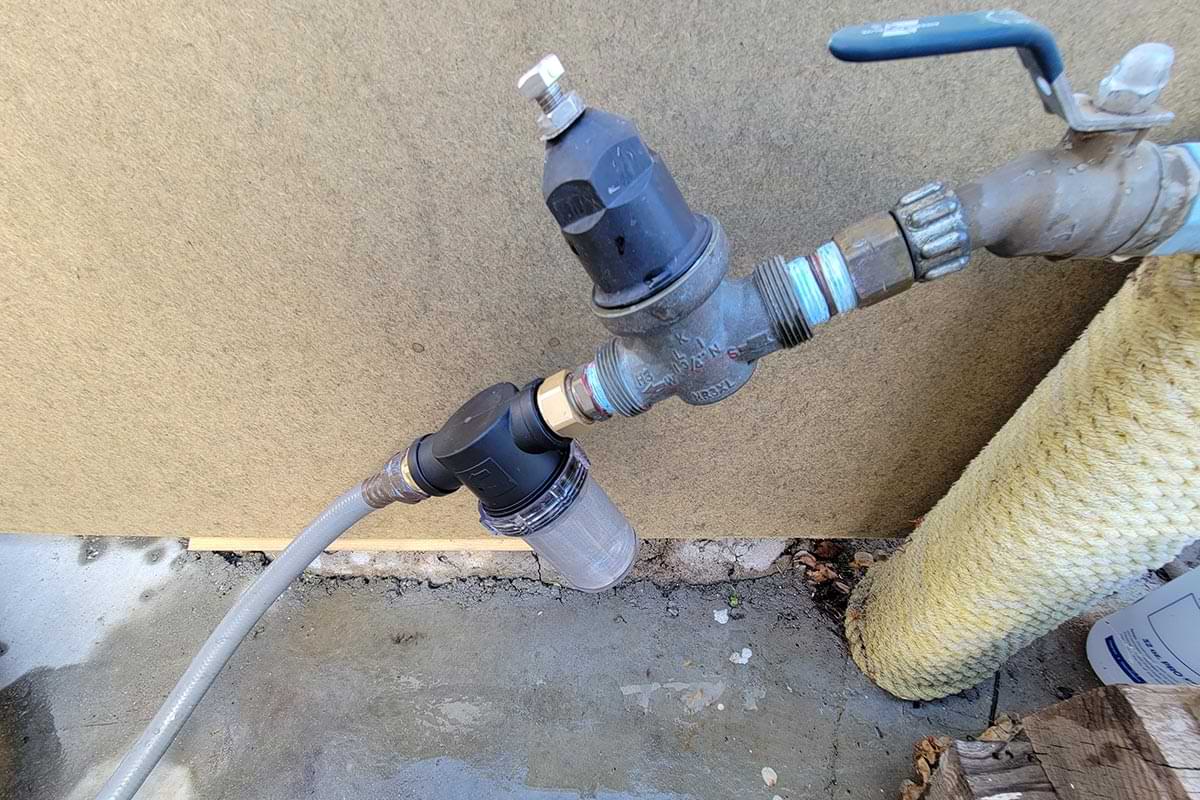 the Twinkle Star Garden Hose Filter Attachment installed between a hose and a water pressure regulator located at the hose bib