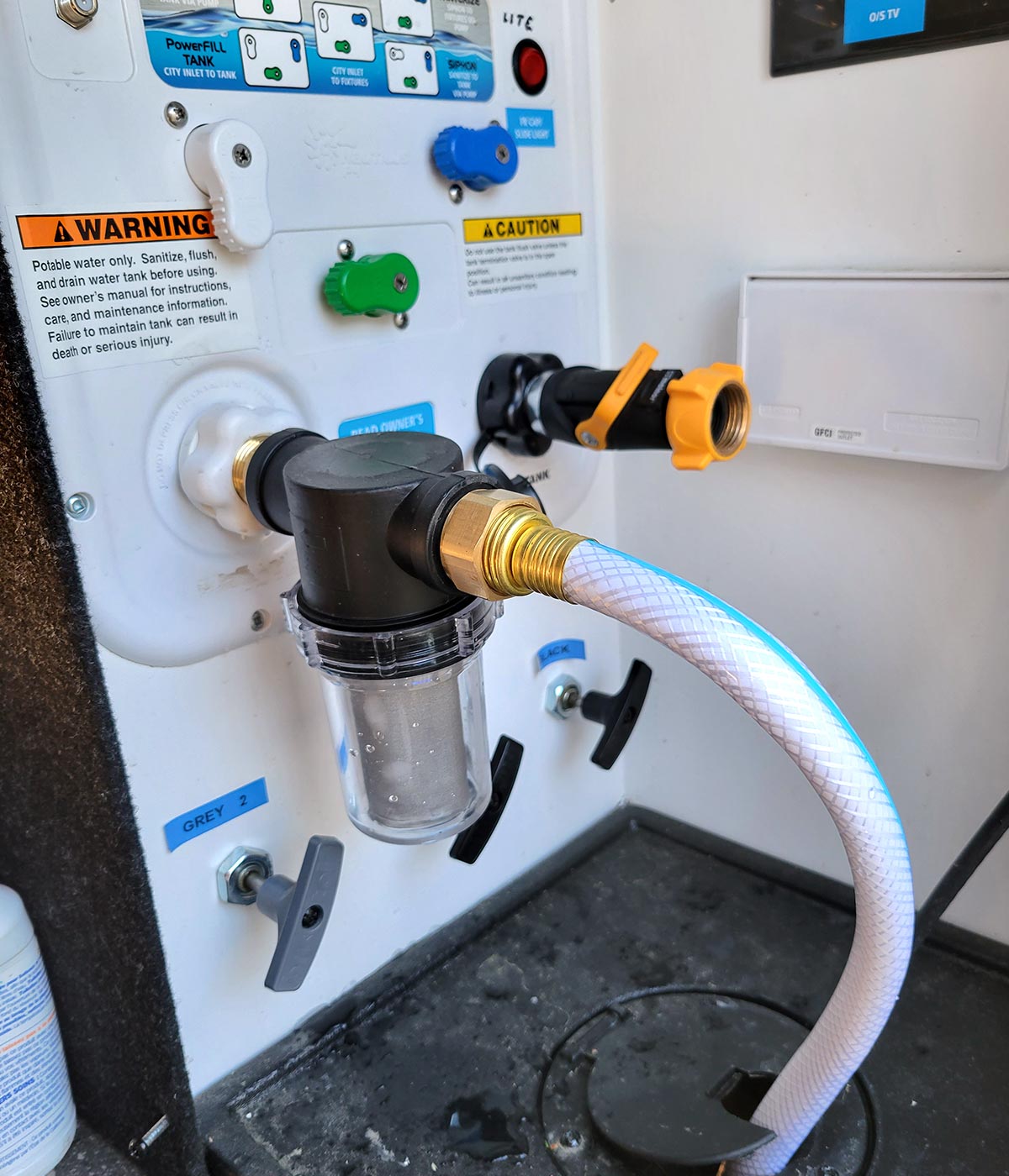 a Twinkle Star Garden Hose Filter Attachment connected directly to the water inlet built into the wall inside the utility bay of an RV