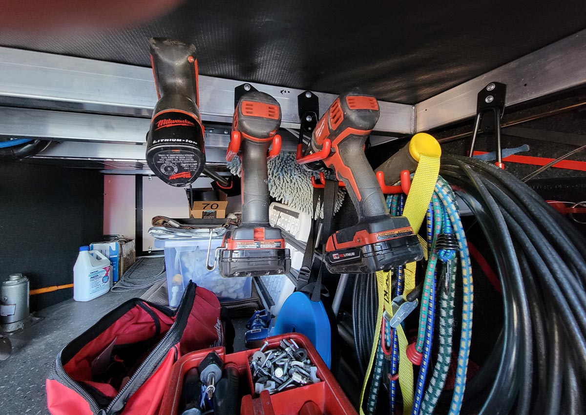 view of the deep external RV compartment with multiple drill guns, bungee cords and electrical cords hanging from TORACK hooks