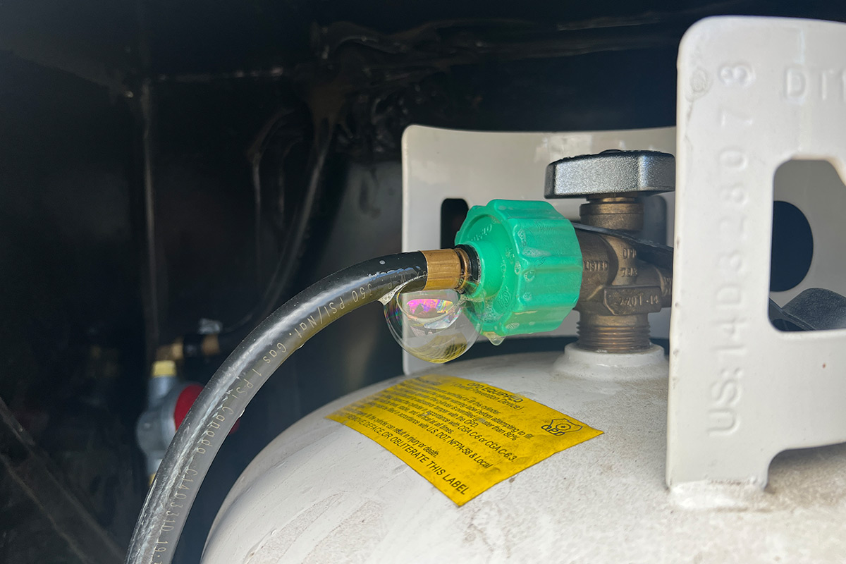 close view of the LP-gas cylinder's fittings and regulator with a large soap bubble at the connection point between the pigtail hose and Type 1 fitting