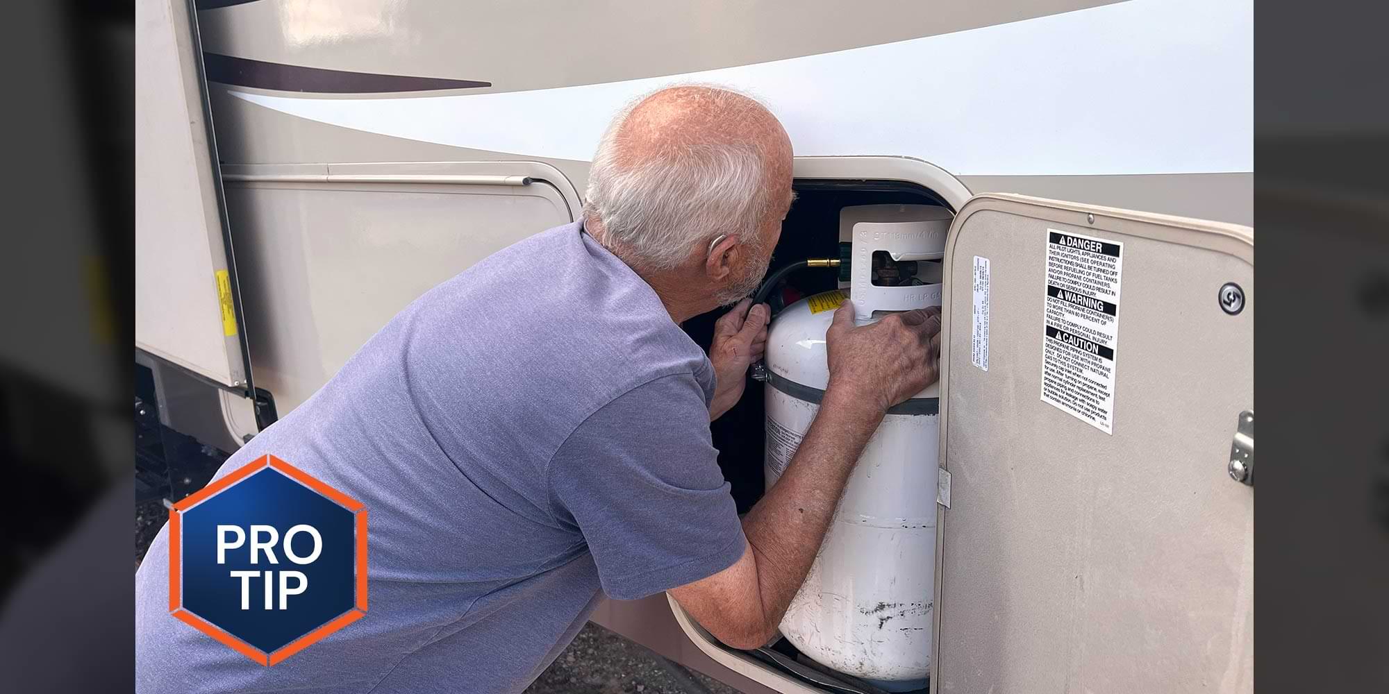 a man leans his head in toward an external RV compartment that holds a gas cylinder