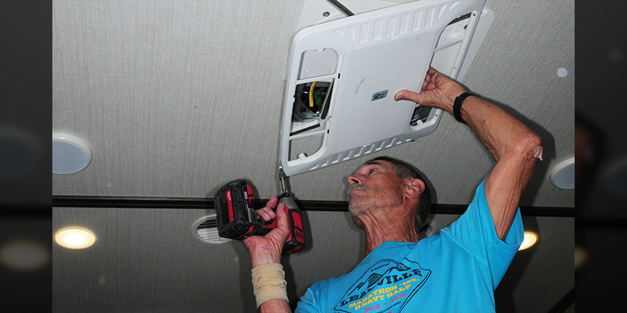 a man uses a drill gun to remove the cover vent from an RV air conditioner