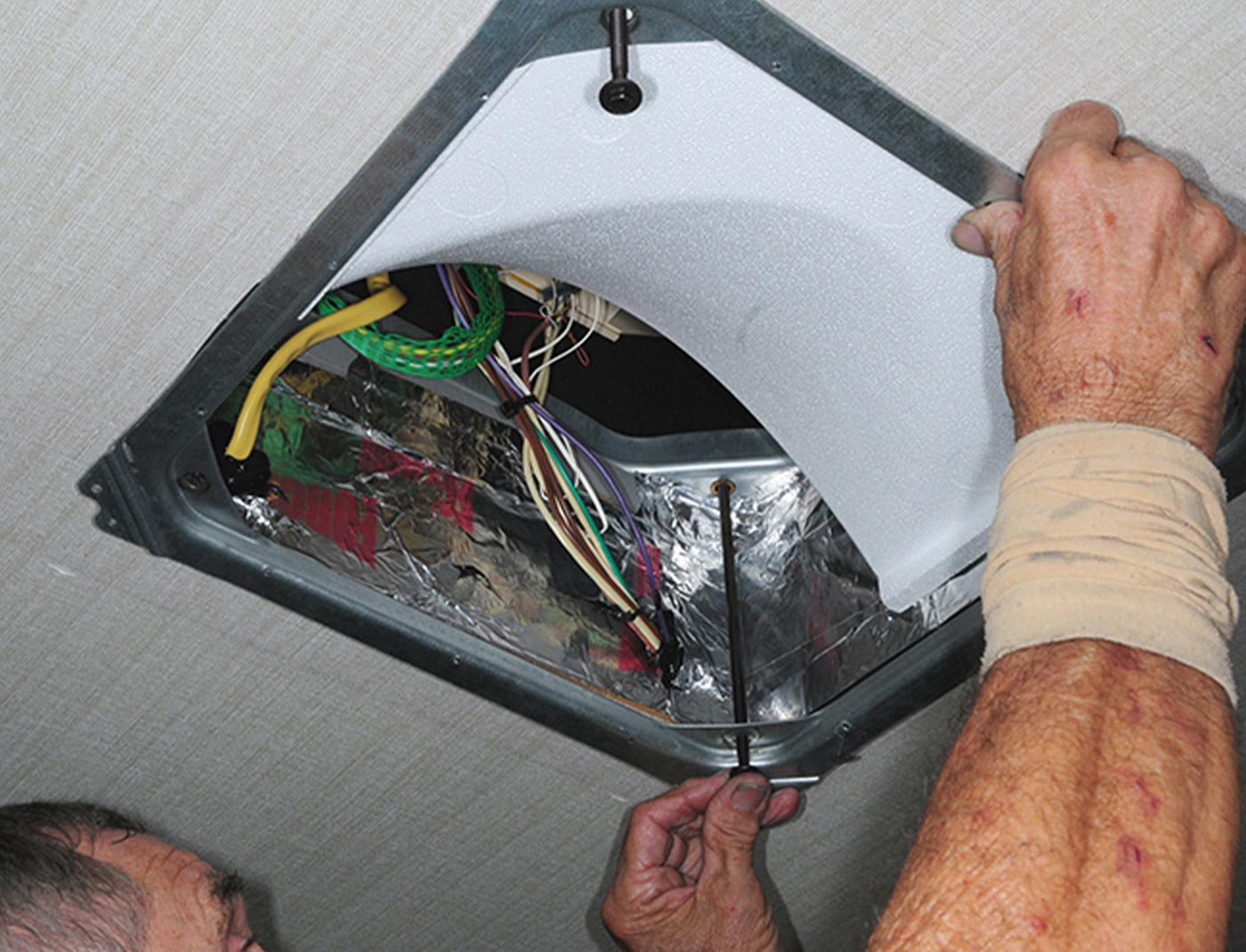 a man adjusts one of four, long hold-down bolts on an RV overhead AC vent opening