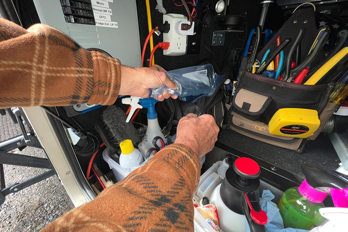 hands place the wrench holding Ziploc bag into an external RV compartment that holds various tools and supplies