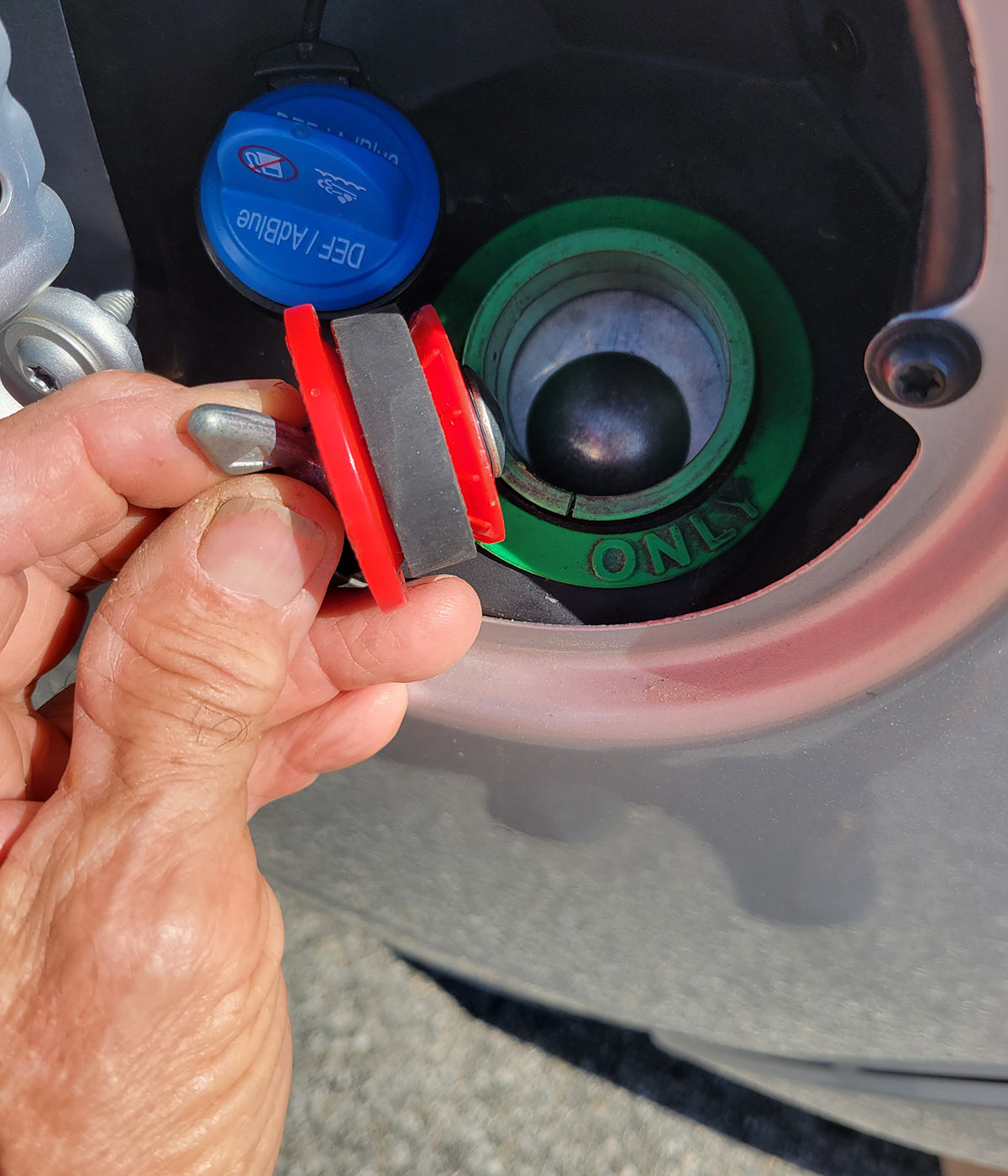 a hand holds an Oatey-brand 1 1⁄2-inch pipe plug for pressure testing beside the fuel filler hole on a Ram diesel-powered truck
