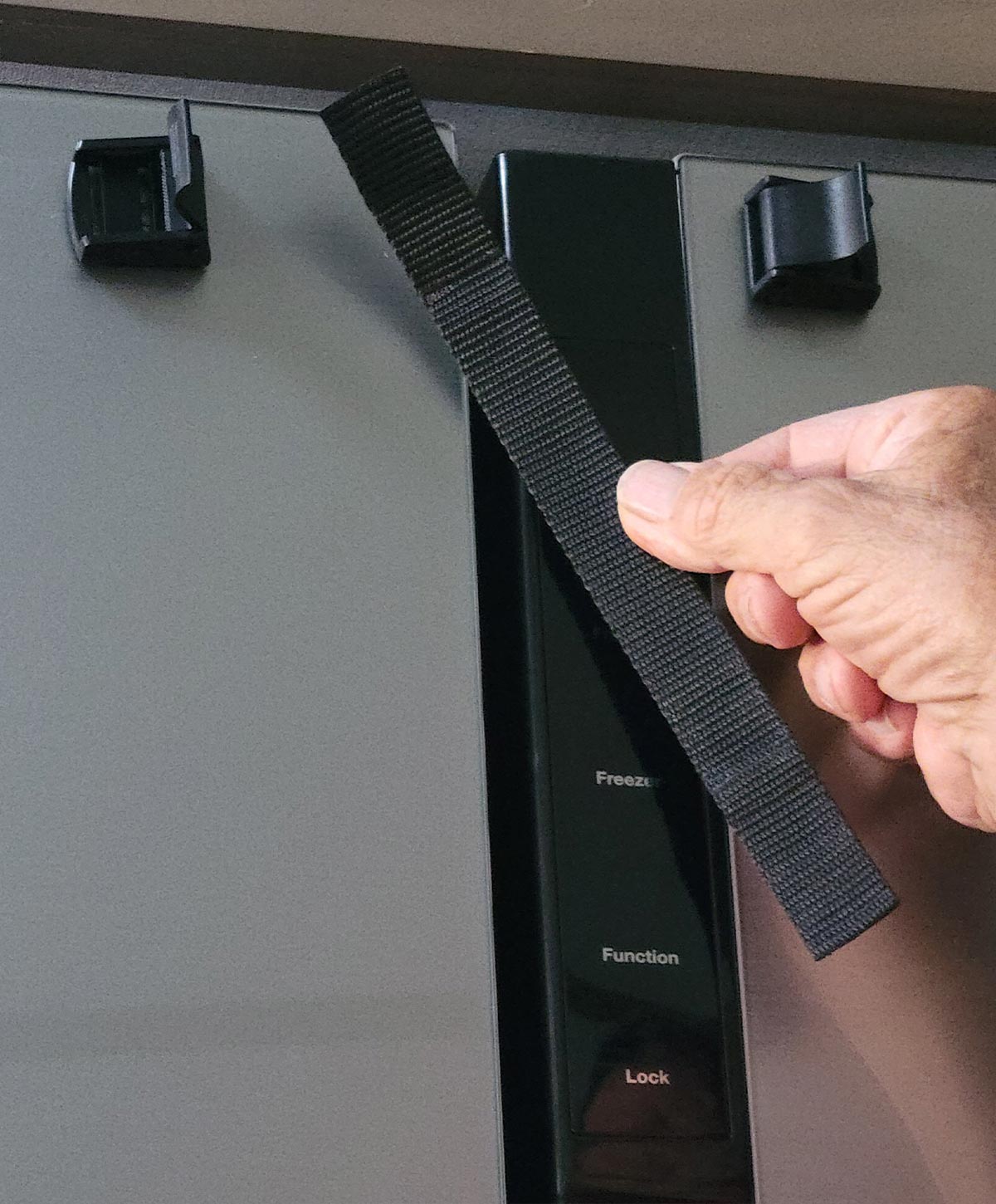 a hand holds the removed strap of the original factory installed refrigerator latch