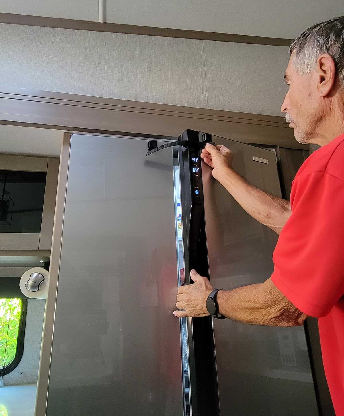 a man holds the latch in mock place with the refrigerator door slightly open, showing how the original latch operated