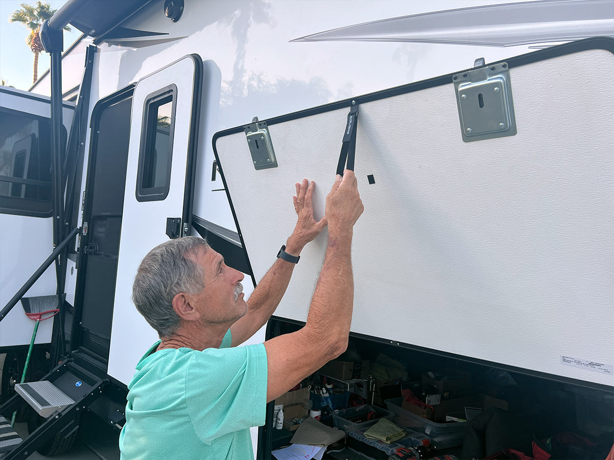 the RV techninican, with a light grasp on the compartment strap, pulls it down to close the compartment door