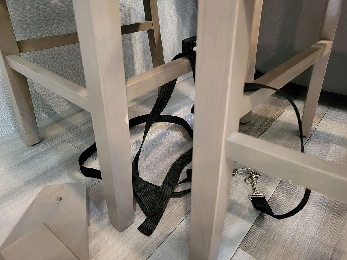 close view of the original chair tiedowns; a jumbled mess of two nylon straps loosely wrapped around the chair legs and connected to two D-rings screwed to the floor