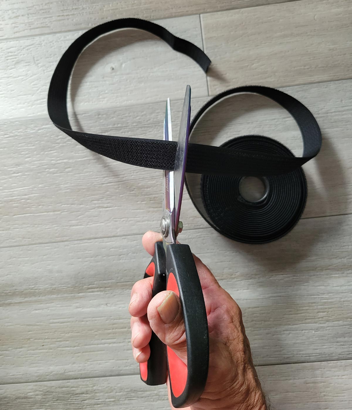 top view of a hand holding scissors and cutting a strap piece from one of the 32.2-foot nylon rolls