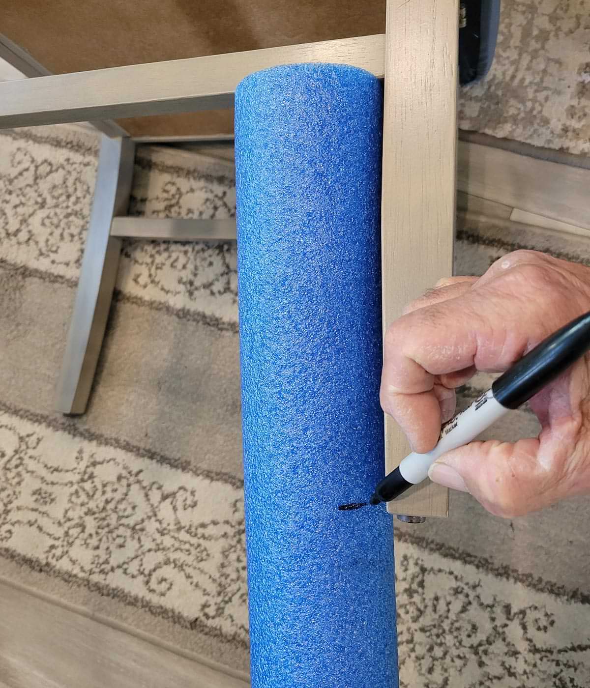 a sharpie is used to mark the horizontal cut location on a bright blue swim noodle held the length of a chair leg, below it's rung